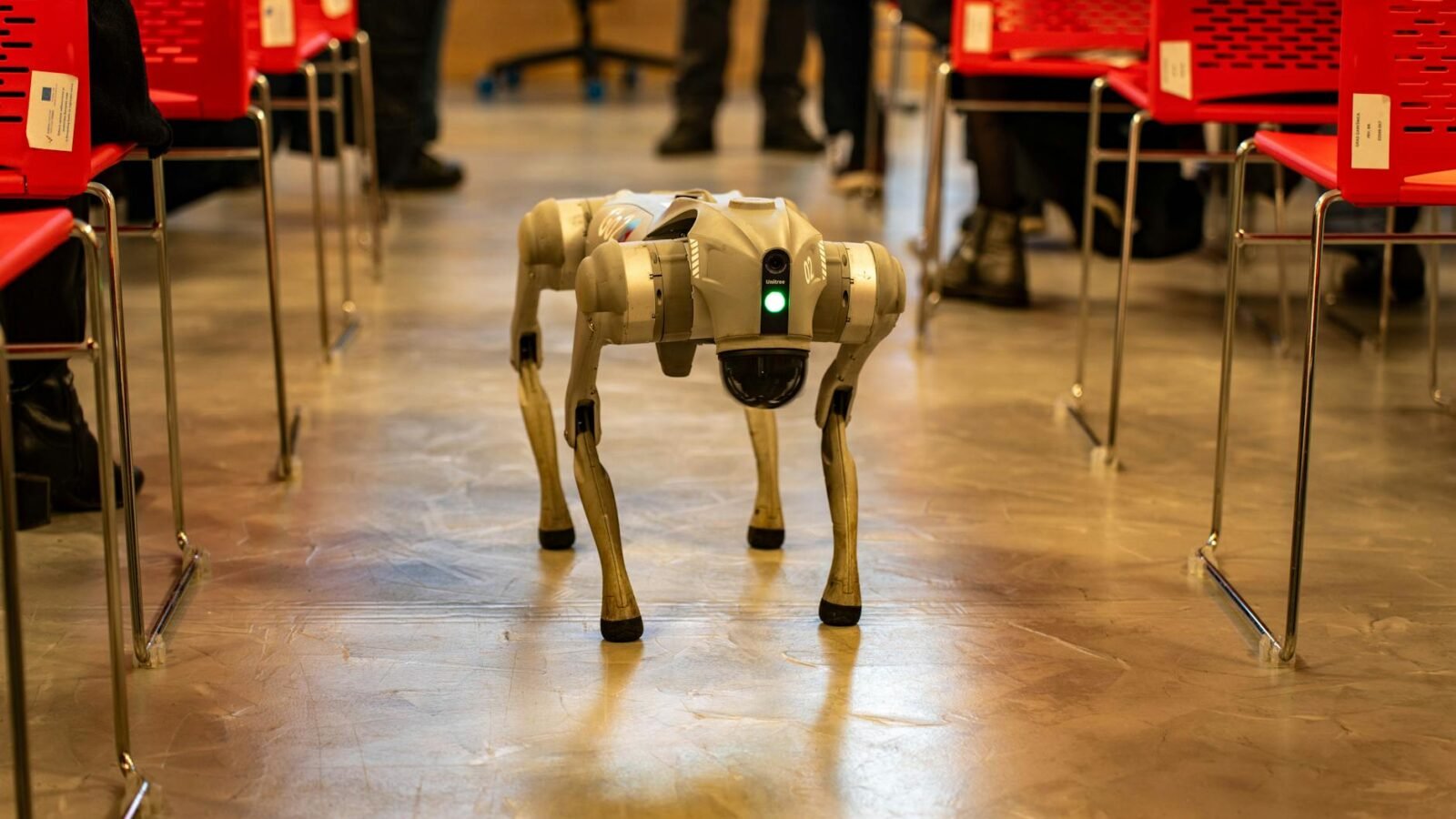 Ein Roboterhund navigiert durch eine Innenumgebung zwischen roten Stühlen und demonstriert Technologie in modernen Umgebungen.