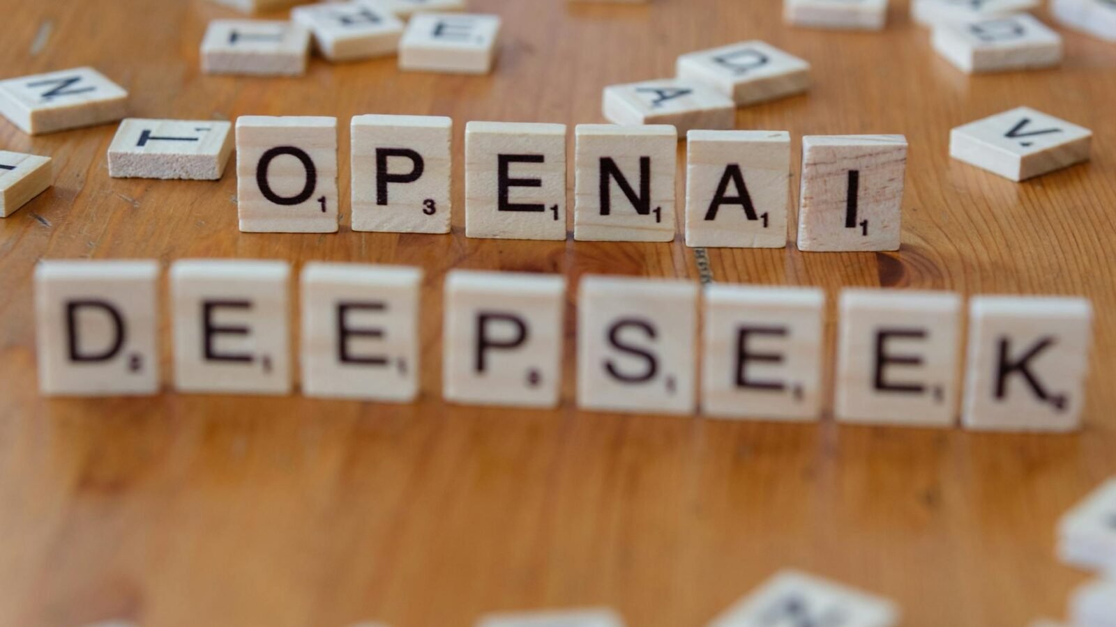 Nahaufnahme von hölzernen Scrabble-Steinen mit den Buchstaben „OpenAI“ und „DeepSeek“ auf einem Holztisch.
