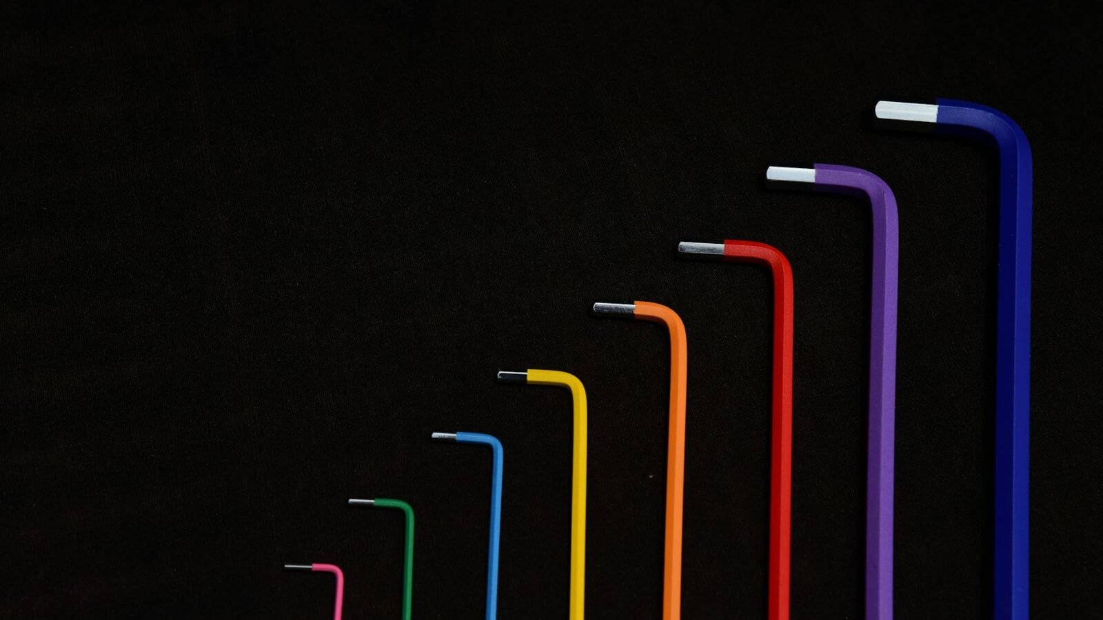 Leuchtende Sechskantschlüssel, nach Größe geordnet, vor dunklem Hintergrund mit einer Regenbogenpalette an Farben.